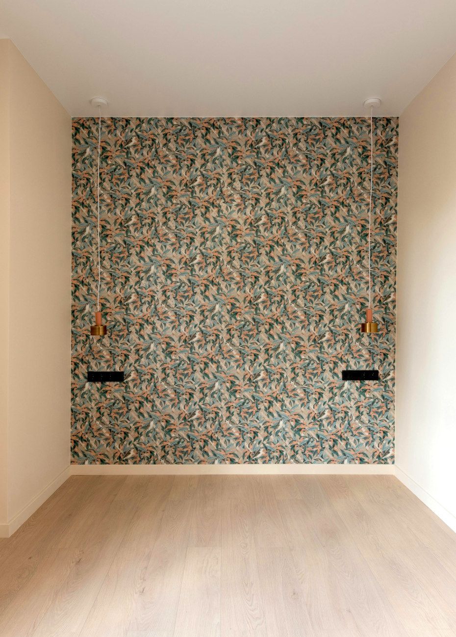 Empty room with patterned wallpaper accent wall, sconces, and wood floor.