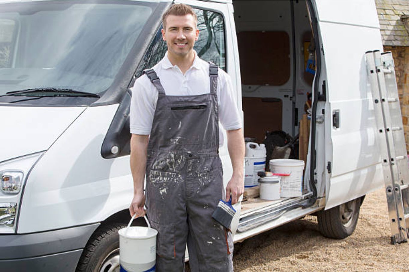 A man is standing in front of a white van holding a bucket of paint.