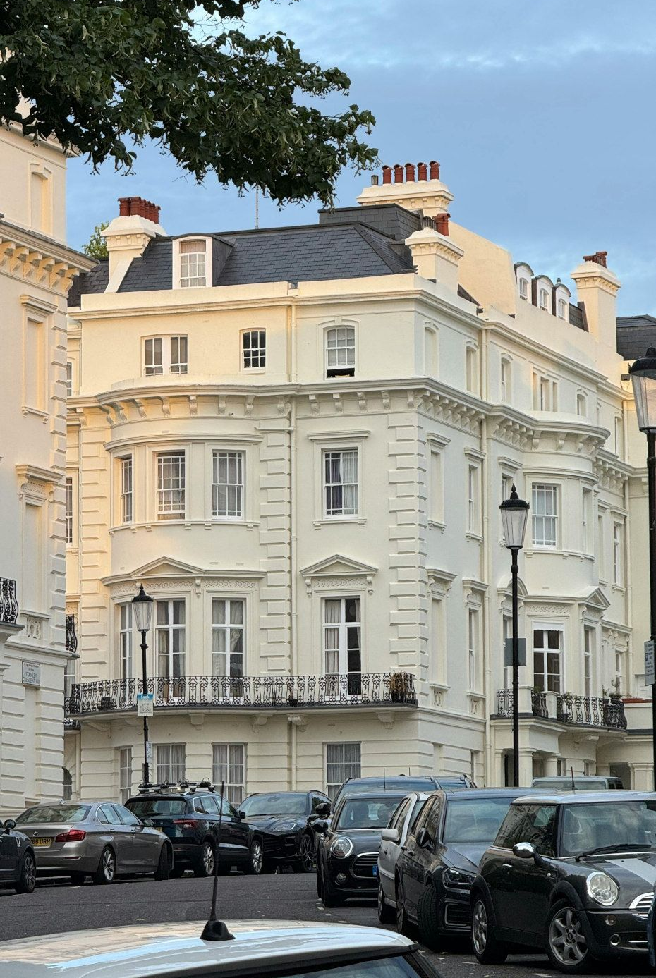 Cream-colored corner building with ornate details, black roof, and parked cars in a London street.