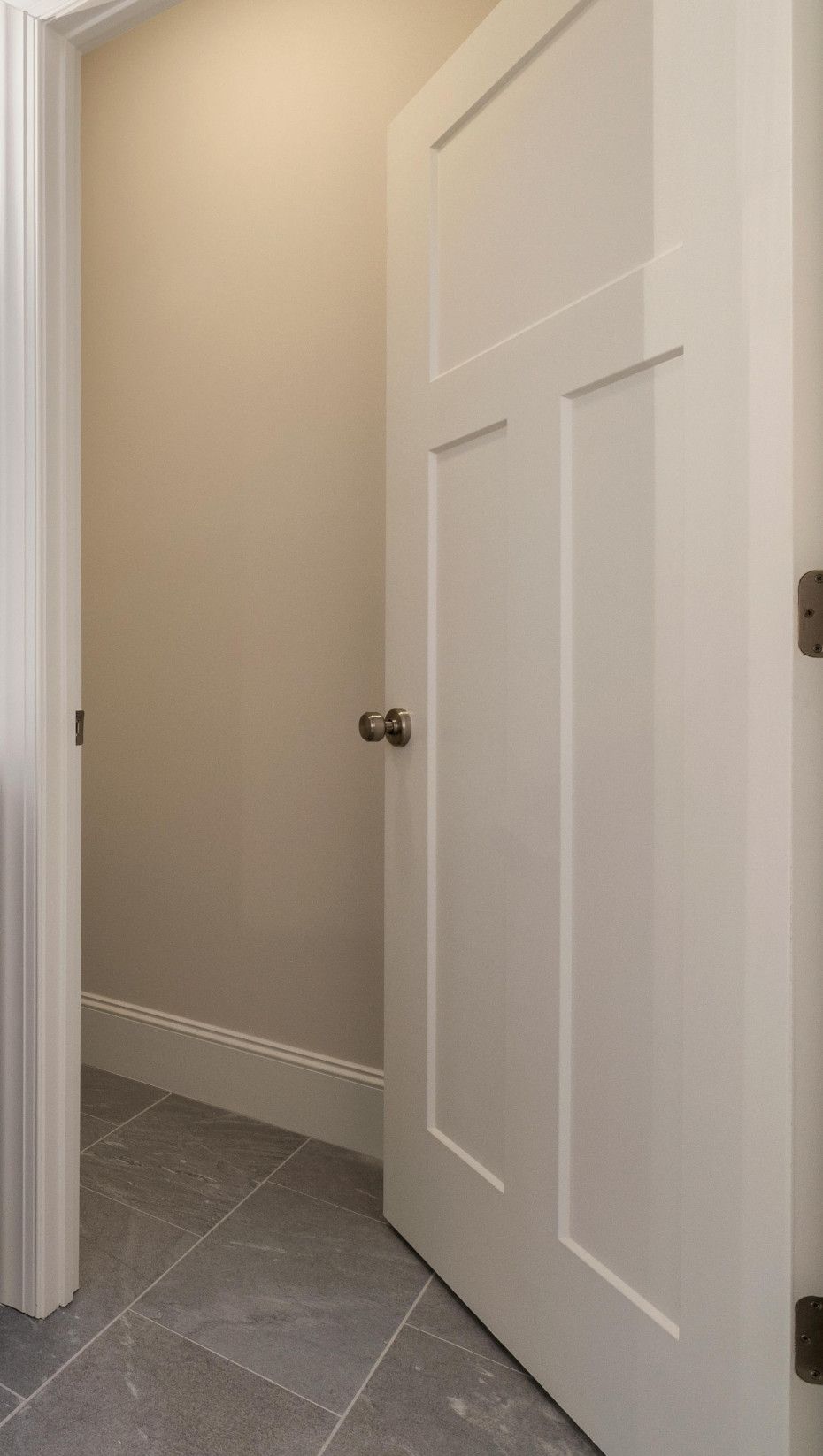 White door ajar in a room with beige walls and tiled floor.