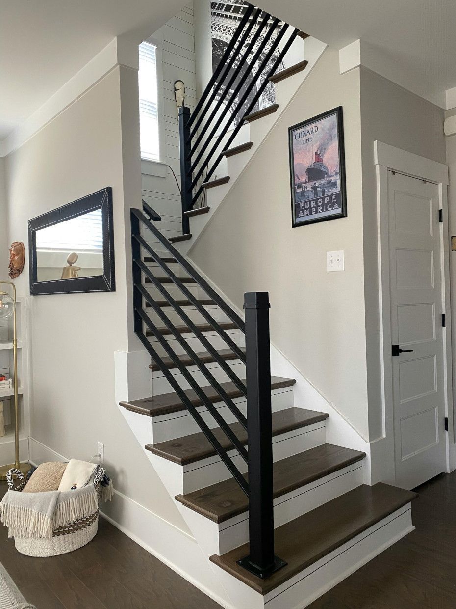 Staircase with black metal railings, white trim, and wood steps. A framed poster and mirror are on the walls.