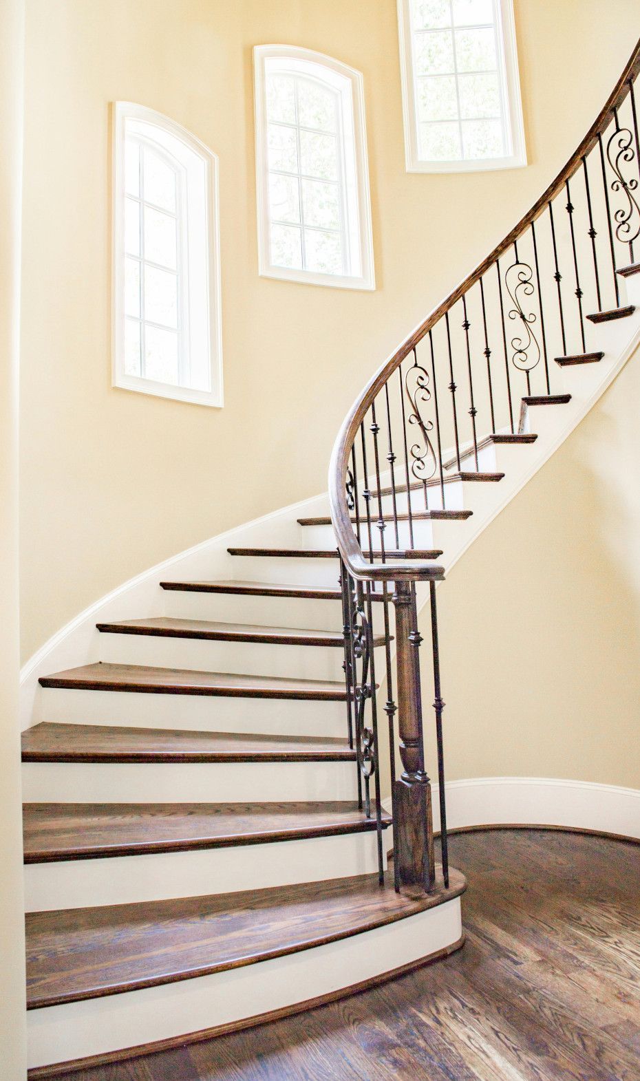 A curved staircase with white risers, dark wood treads, and an ornate black iron railing.
