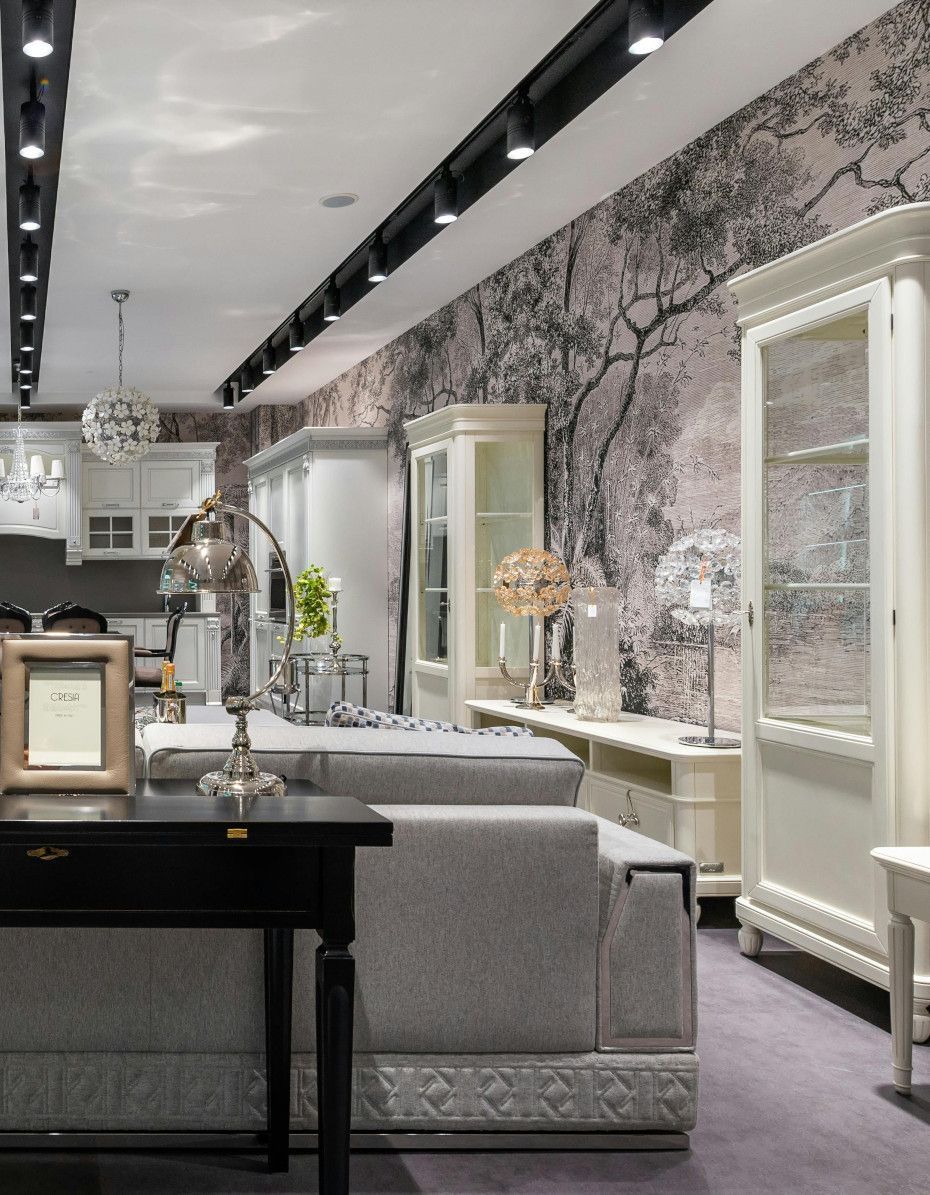 Furniture showroom with white cabinetry, grey sofa, and a nature-themed wallpaper backdrop.