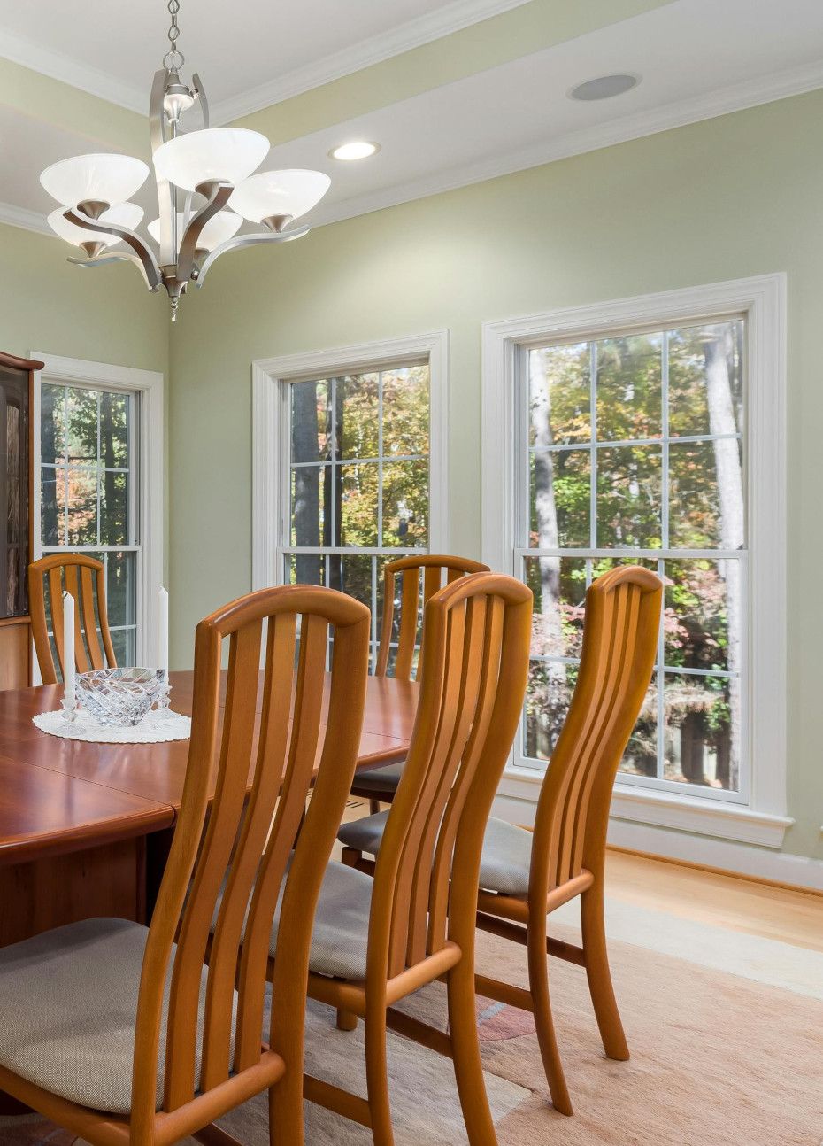 Dining room with wooden table, chairs, and windows overlooking trees; chandelier overhead.