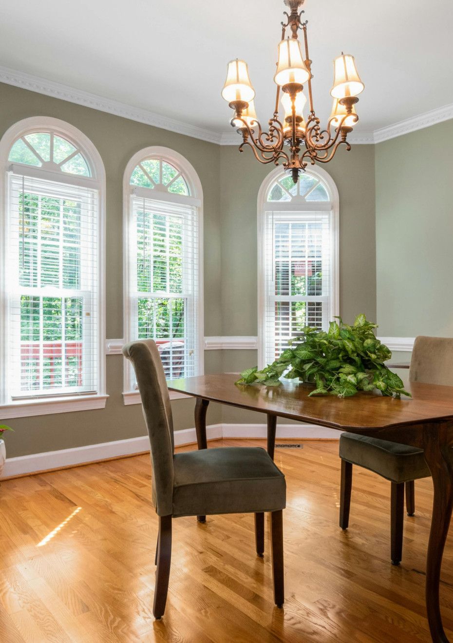 Dining room with wooden table, chairs, and arched windows. Green walls, chandelier, and natural light.
