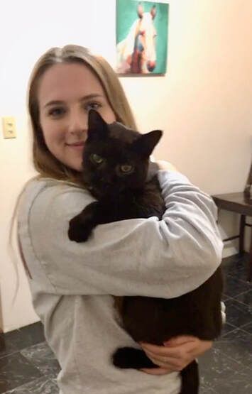 A woman is holding a black cat in her arms.