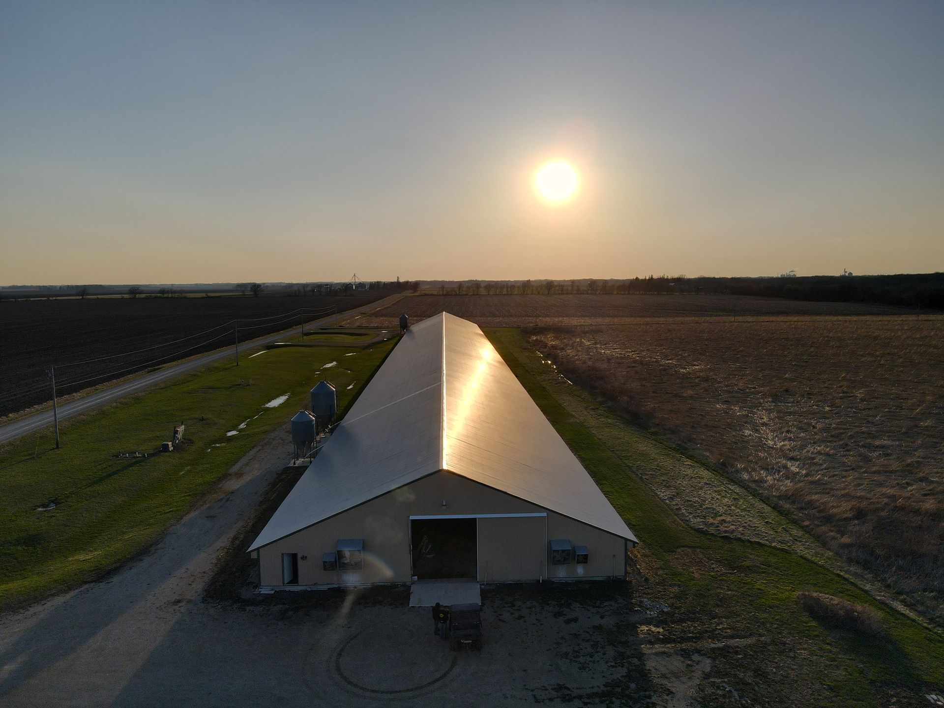 Sunlit farm building with a metal roof between fields at sunset.