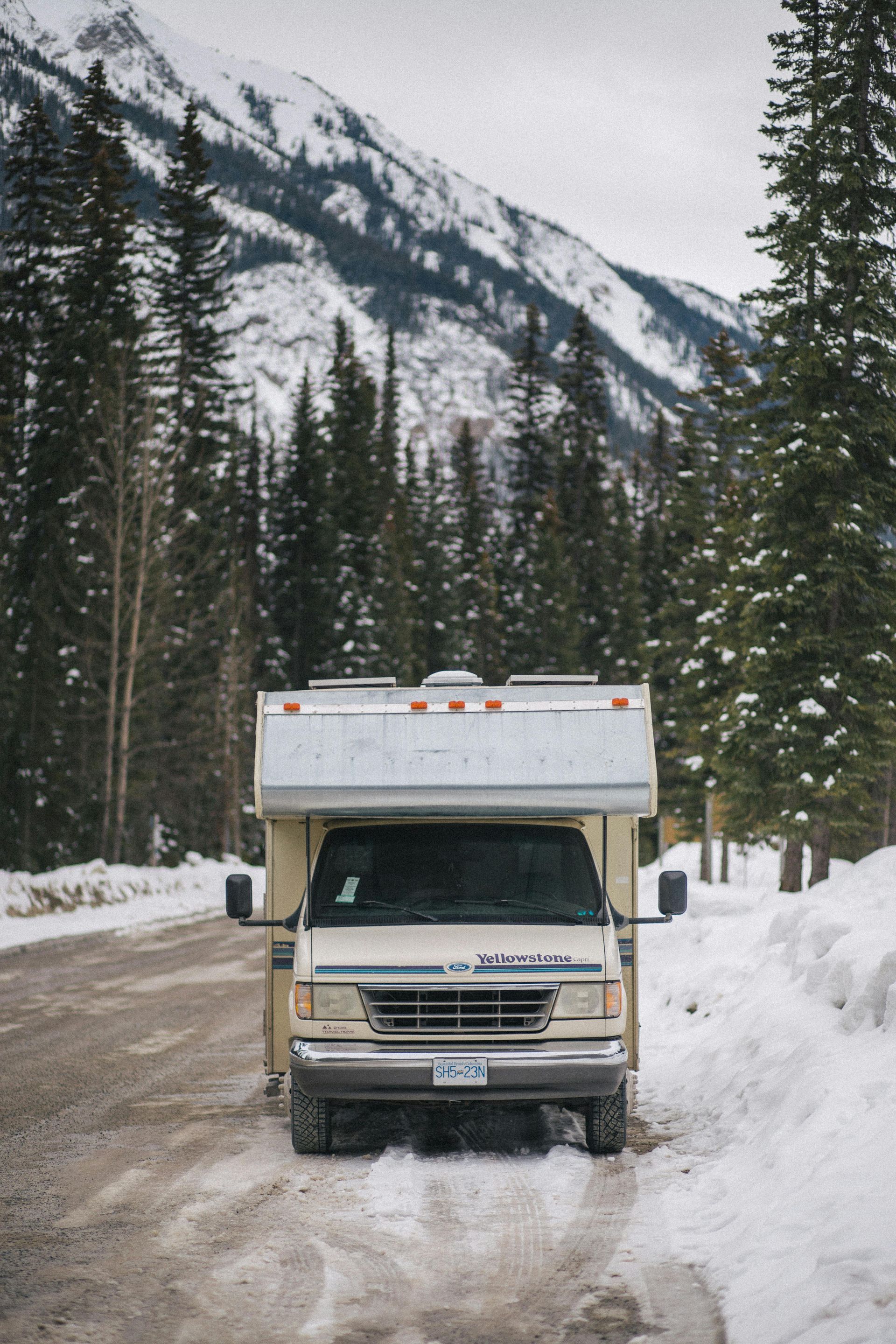 RV parked on a snowy road in a mountain forest. Snow on ground and trees.