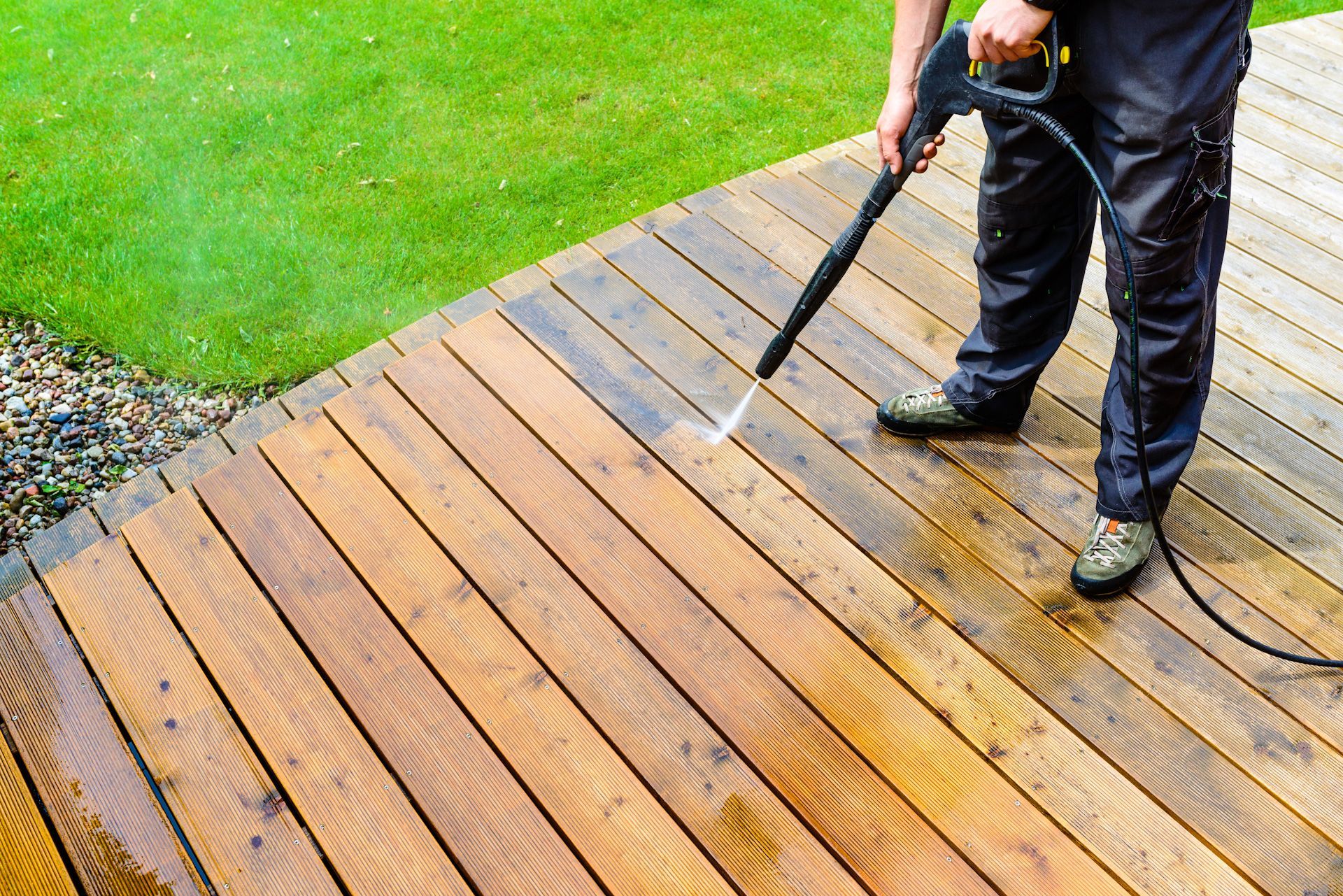 A man is cleaning a wooden deck with a high pressure washer.