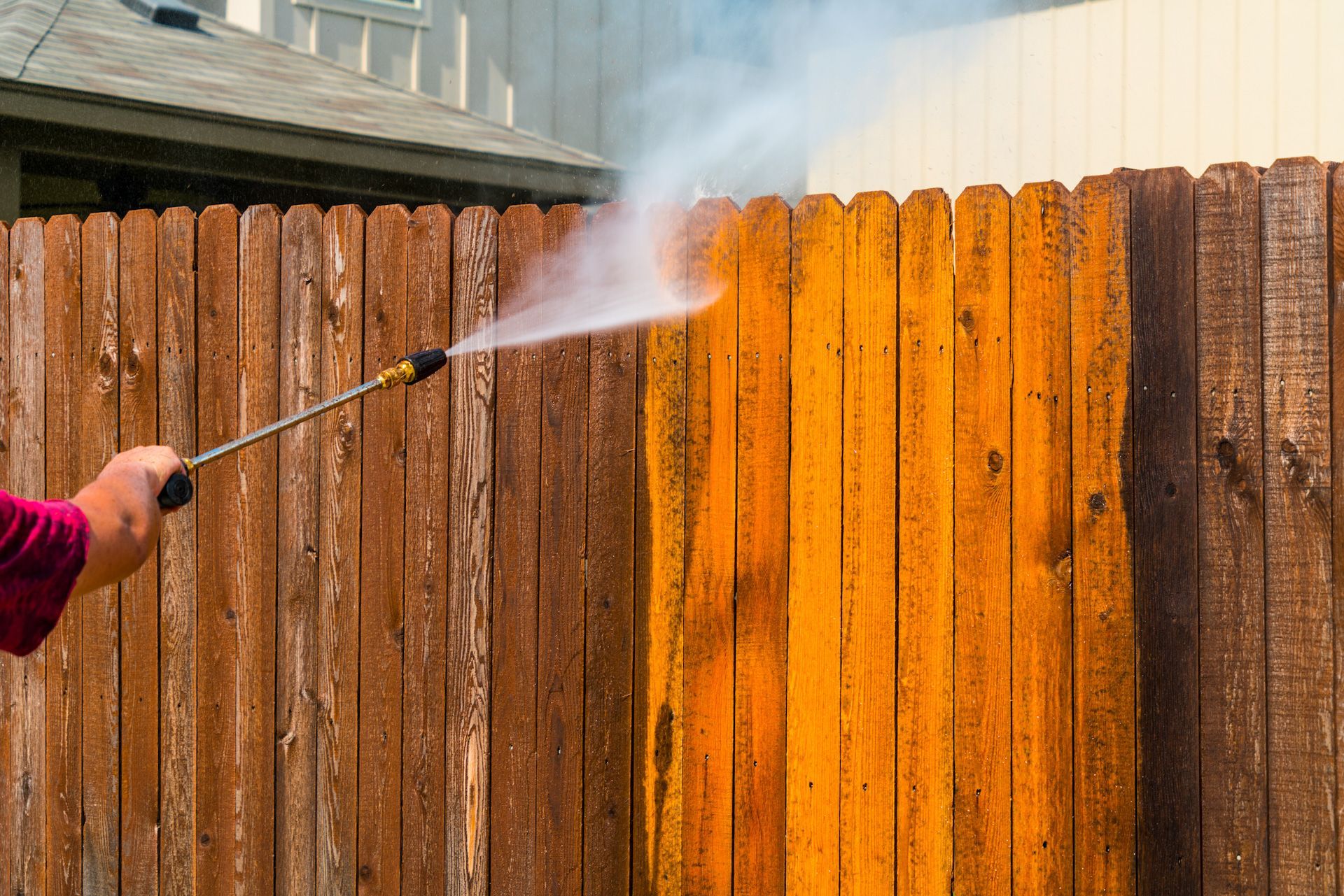 A person is using a high pressure washer to clean a wooden fence.