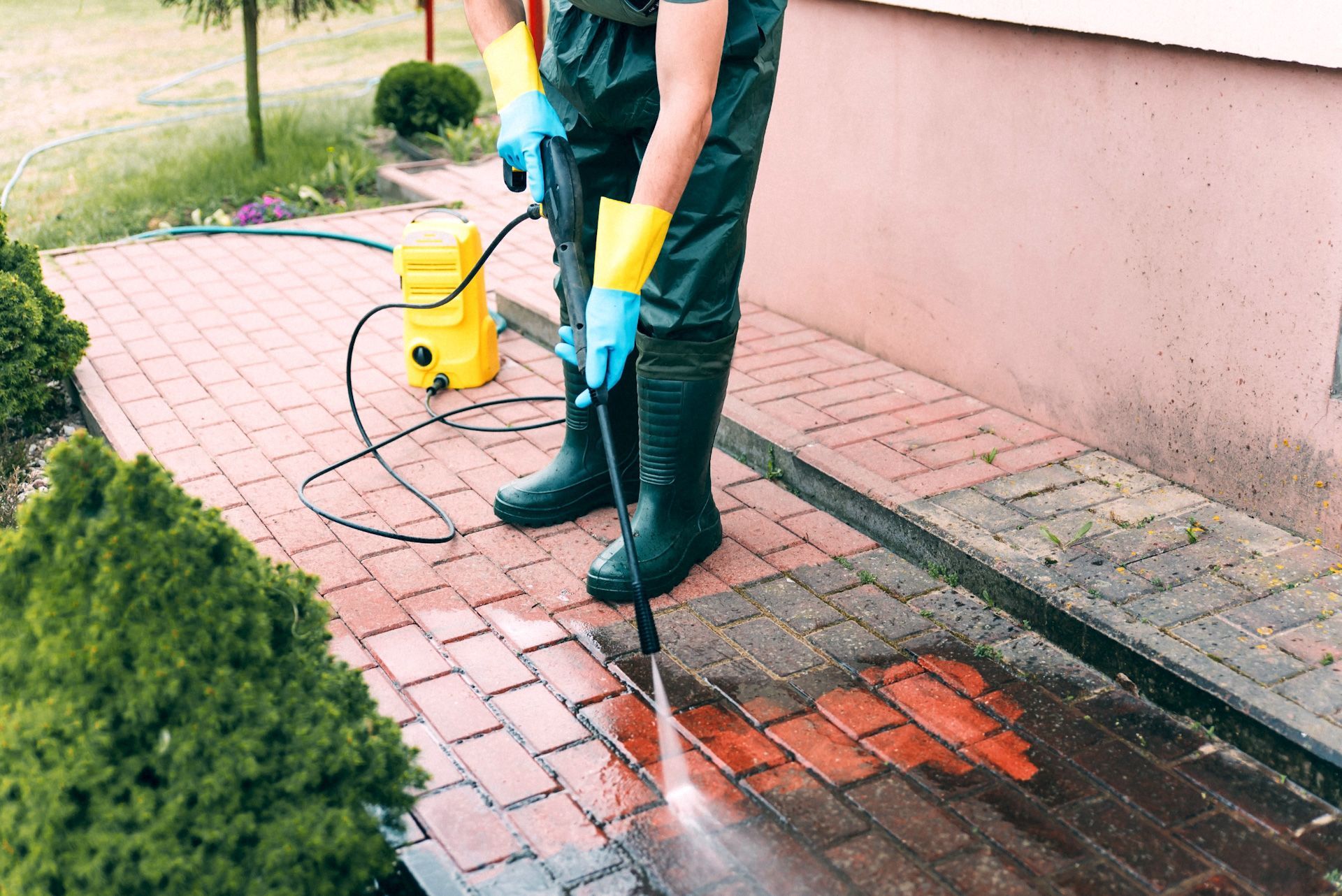 A man is cleaning a sidewalk with a high pressure washer.