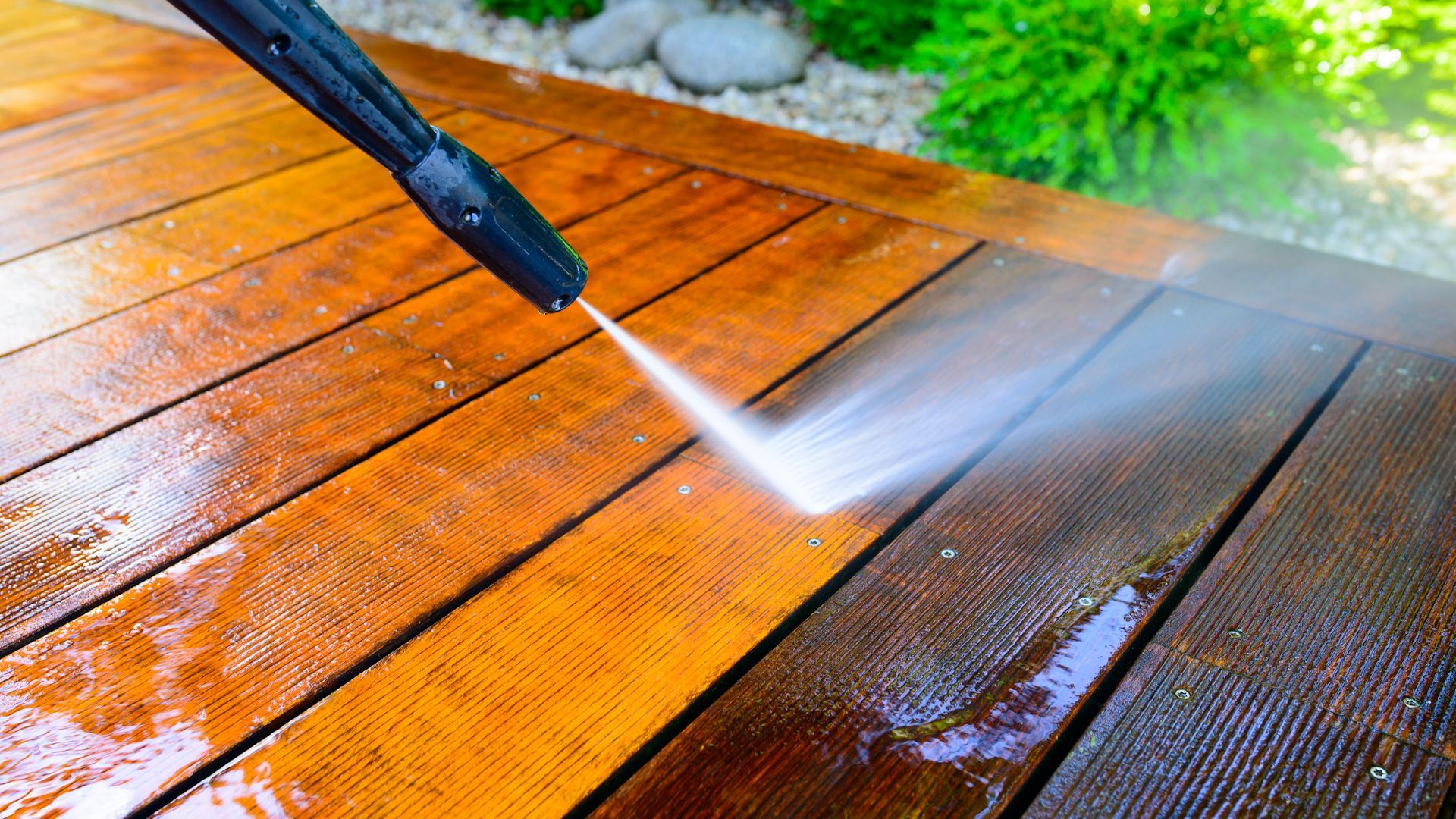 A person is using a high pressure washer to clean a wooden deck.