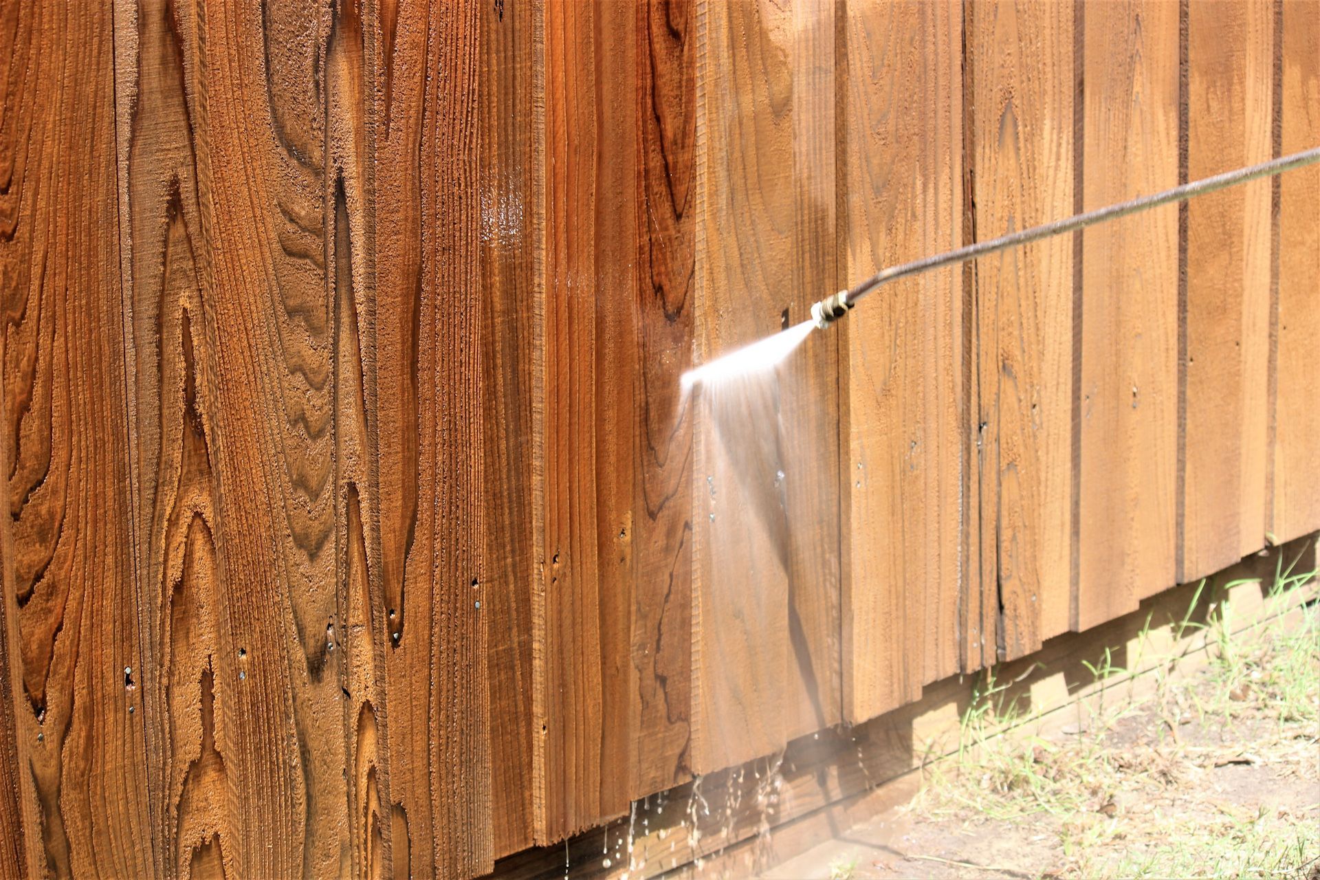 A person is cleaning a wooden fence with a high pressure washer.