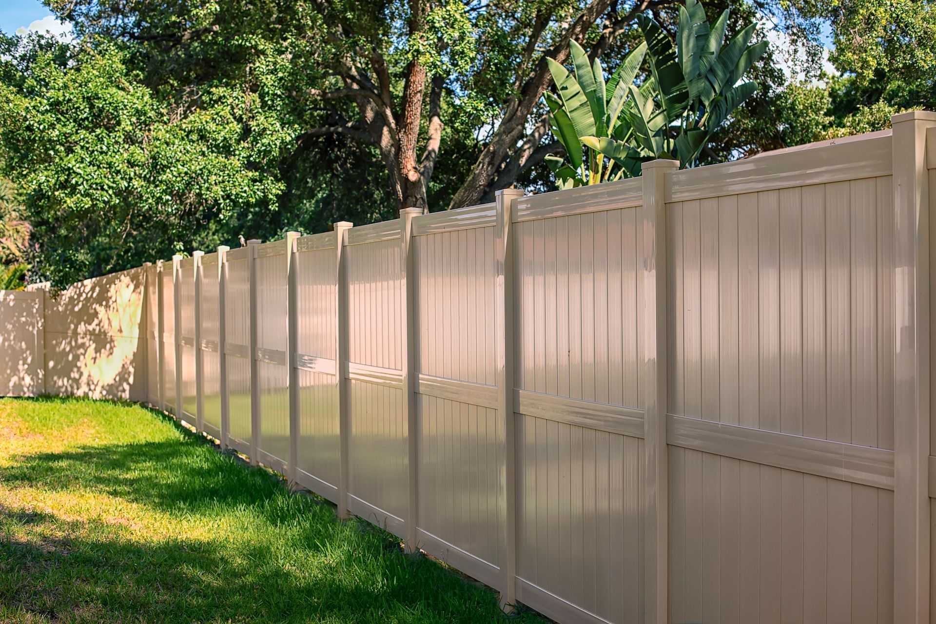 A tan vinyl fence surrounds a lush green yard.