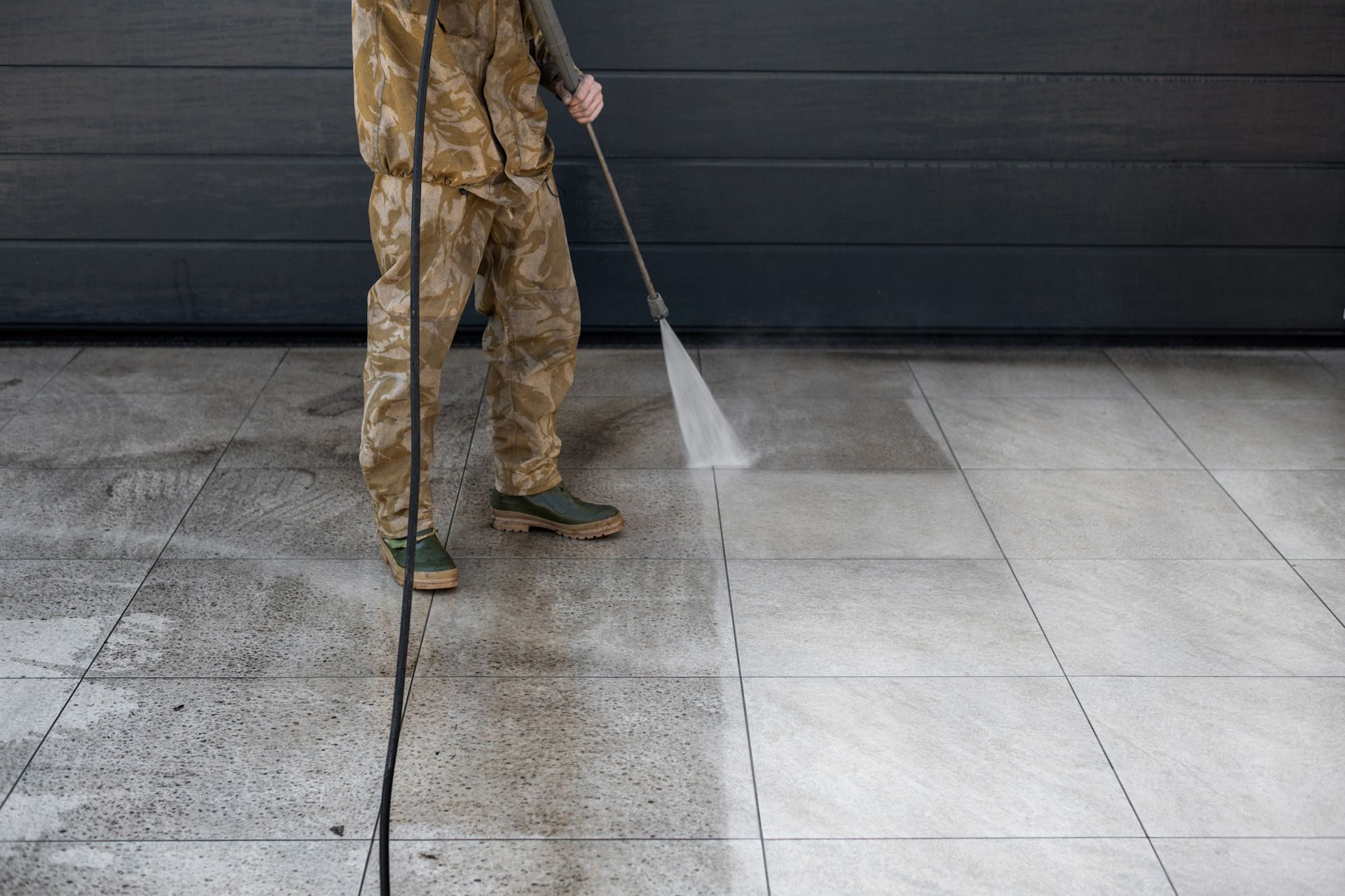 A man is cleaning a concrete floor with a high pressure washer.