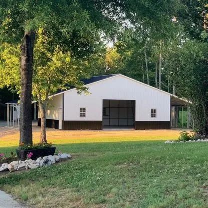 A large white barn is sitting in the middle of a lush green field surrounded by trees.