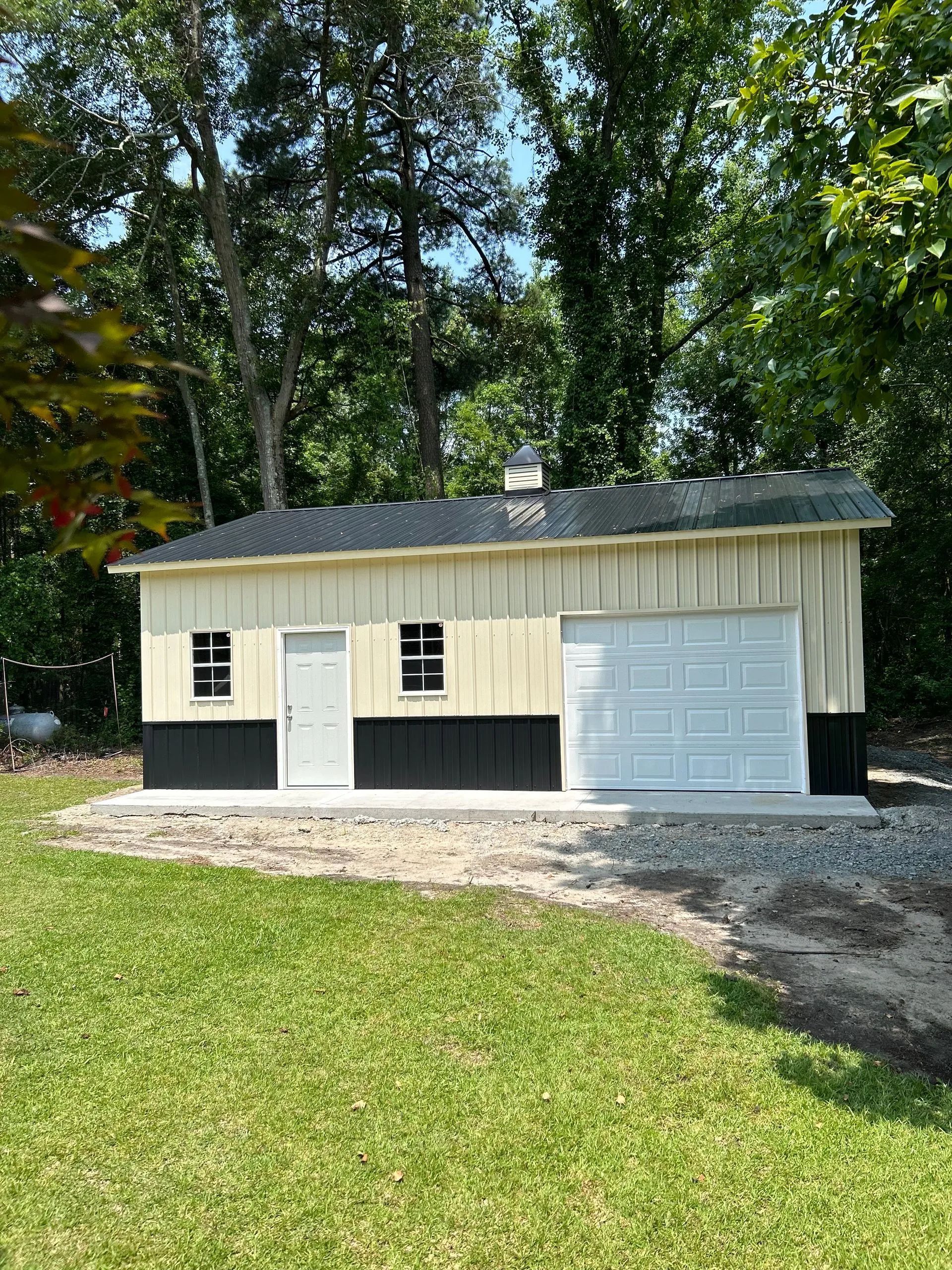A white and black garage with a black roof is sitting in the middle of a lush green field.