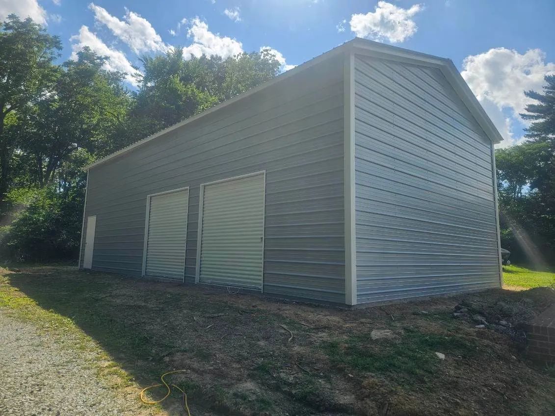 A large metal garage with two doors is sitting in the middle of a grassy field.