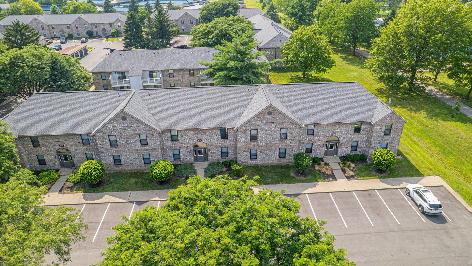 Stone-faced apartment buildings with angled roofs, surrounded by trees and a parking lot.