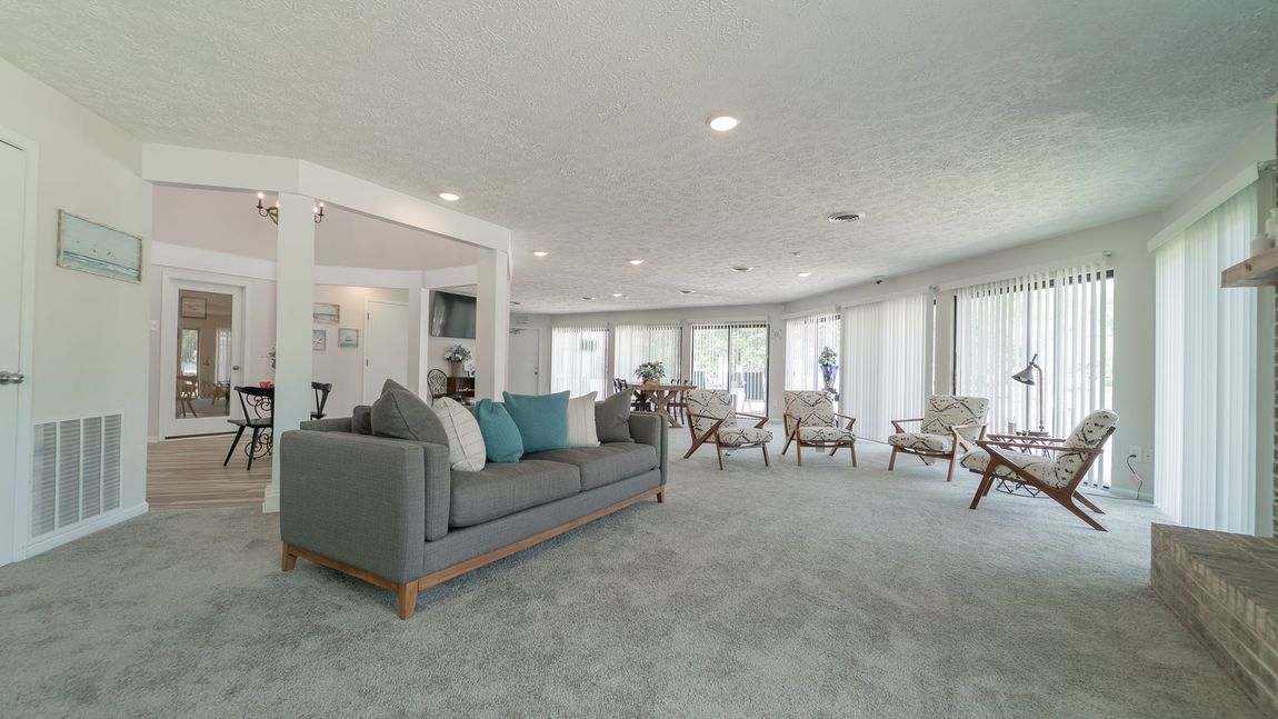 Spacious living room with gray sofa, armchairs, and large windows. Light blue pillows.