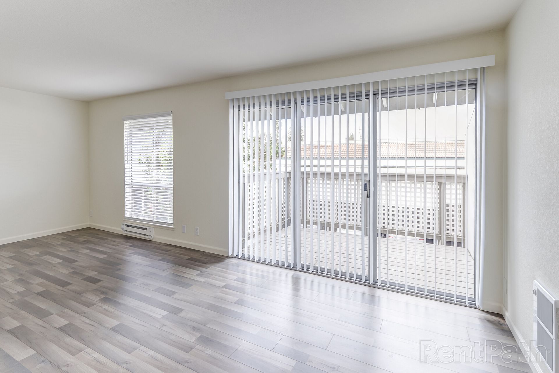 An empty living room with hardwood floors and sliding glass doors leading to a balcony.