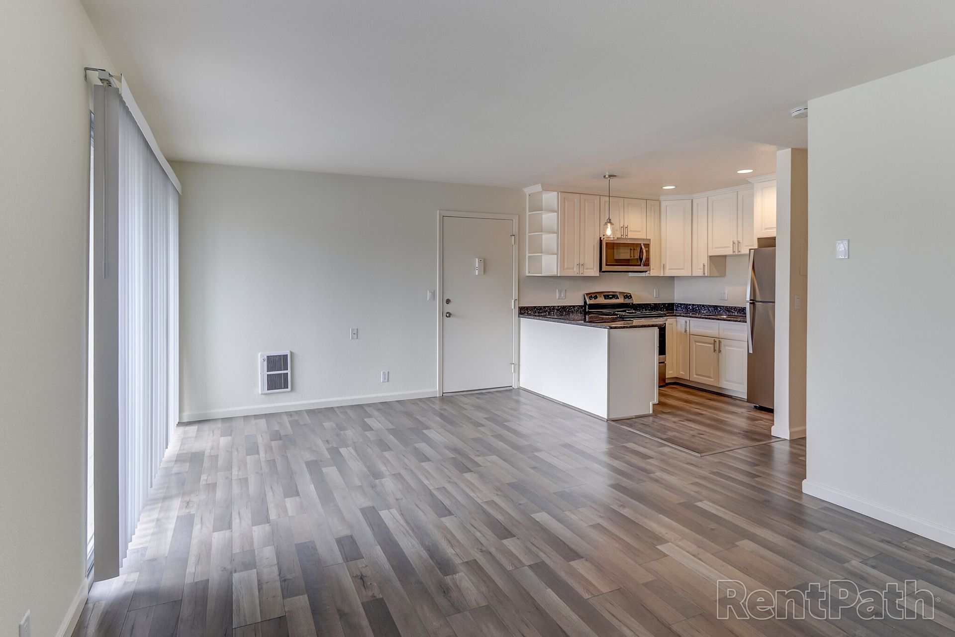 A living room with hardwood floors and a kitchen in the background.