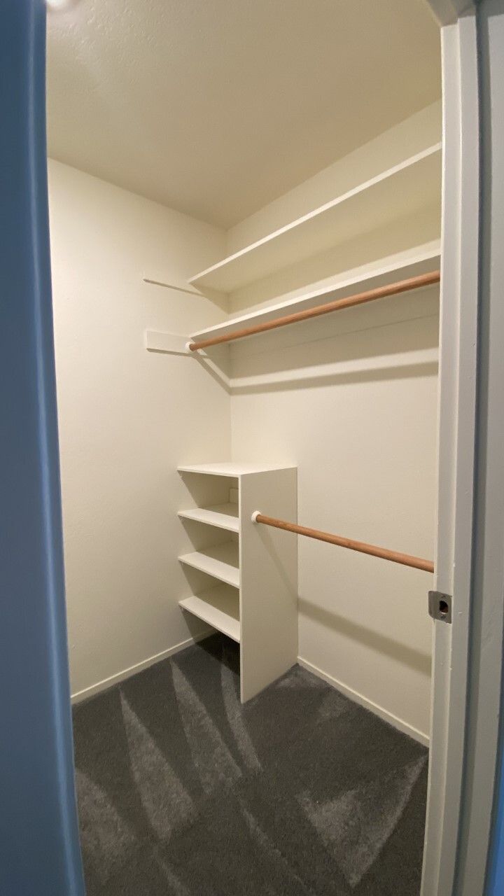 A walk in closet with shelves and a wooden railing.