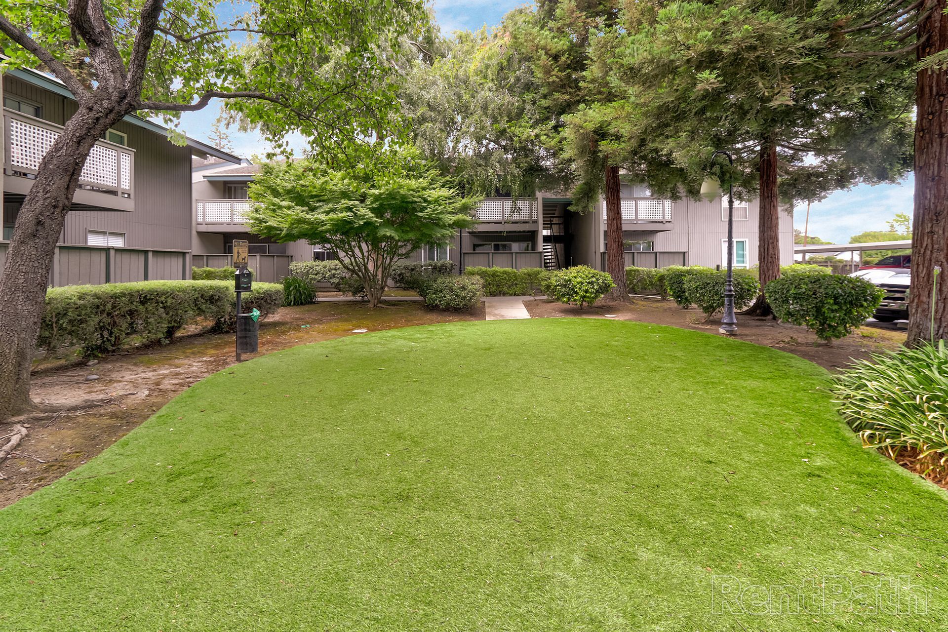 A large lush green lawn in front of a building with trees and bushes.