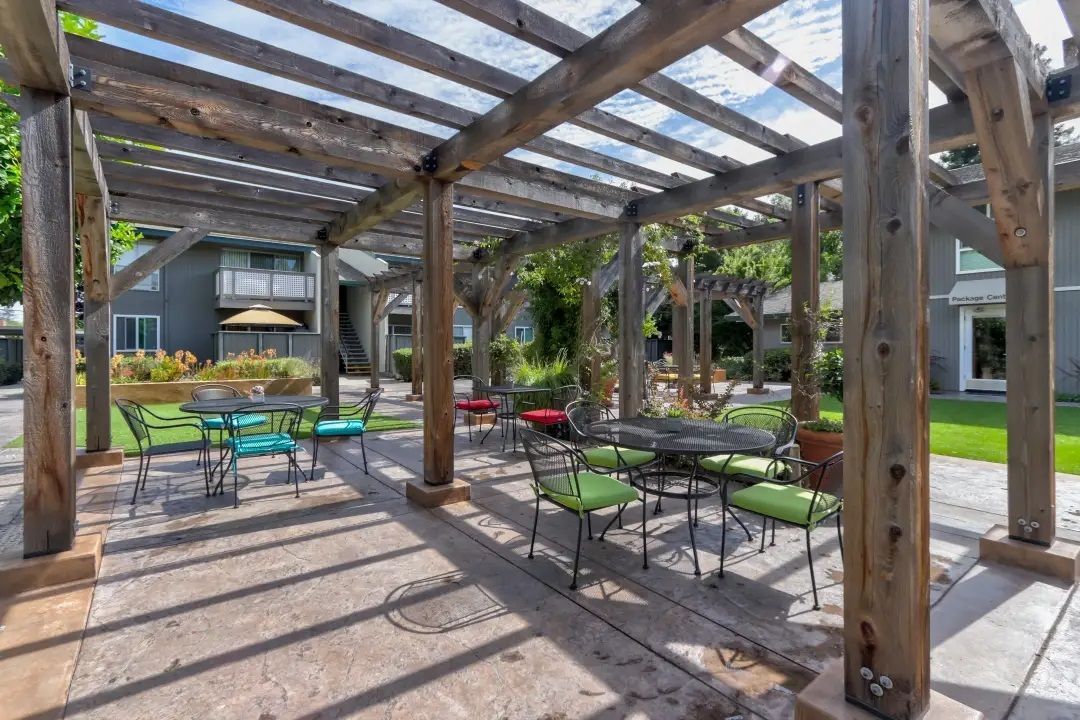 A wooden pergola with tables and chairs underneath it.