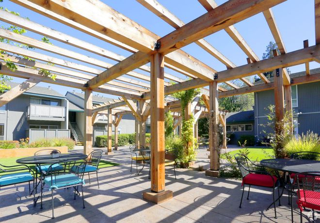 A patio with tables and chairs under a wooden pergola.