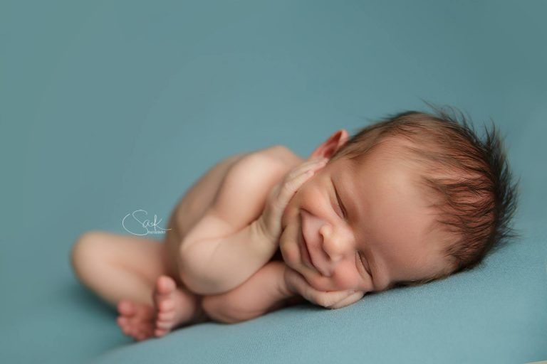 A newborn baby is smiling while sleeping on a blue blanket.