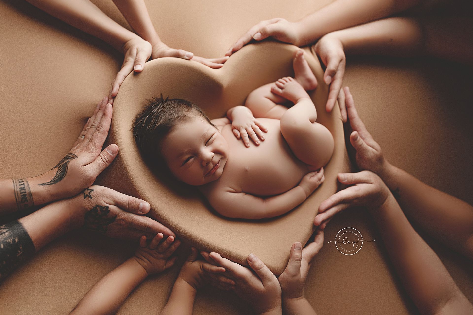 A group of people are holding a newborn baby in a heart shaped bowl.