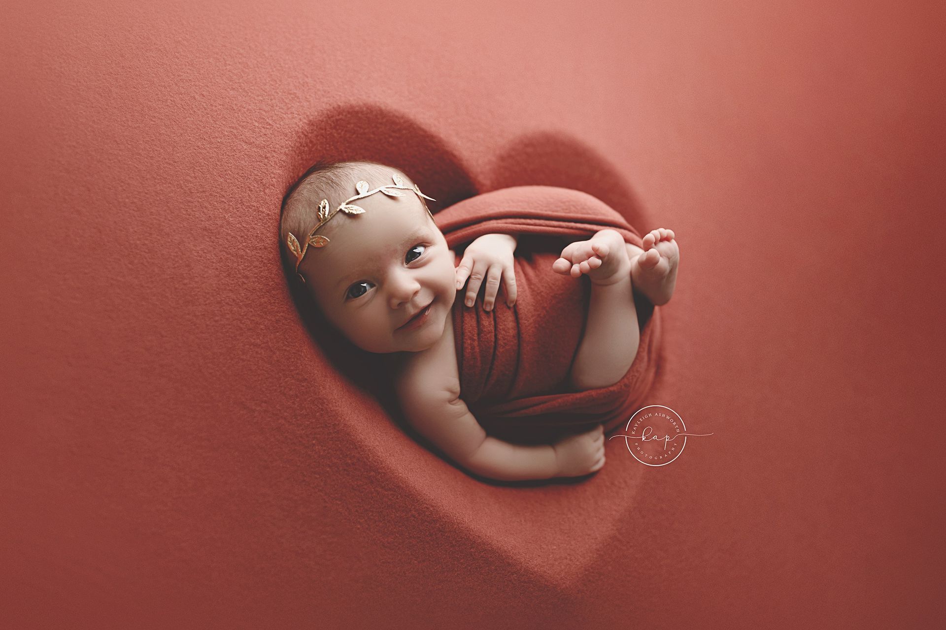 A newborn baby is laying in a heart shaped blanket.