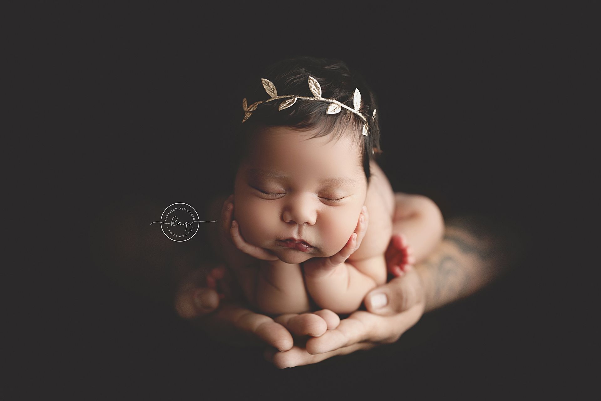 A newborn baby girl wearing a headband is being held in a person 's hands.