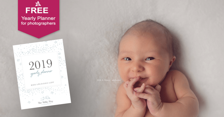 A baby is laying next to a free yearly planner for photographers