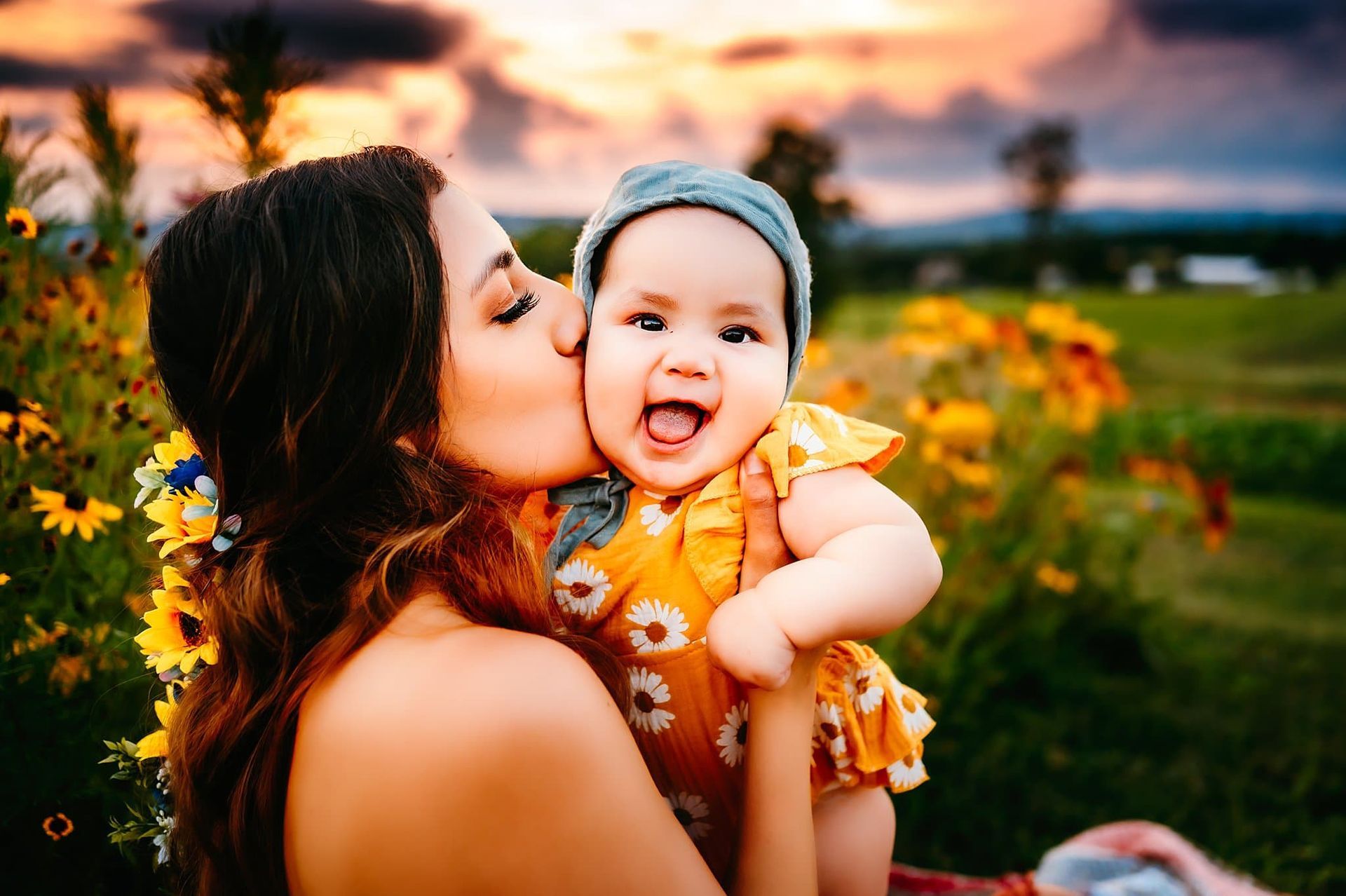 A woman is kissing a baby on the cheek in a field of flowers.