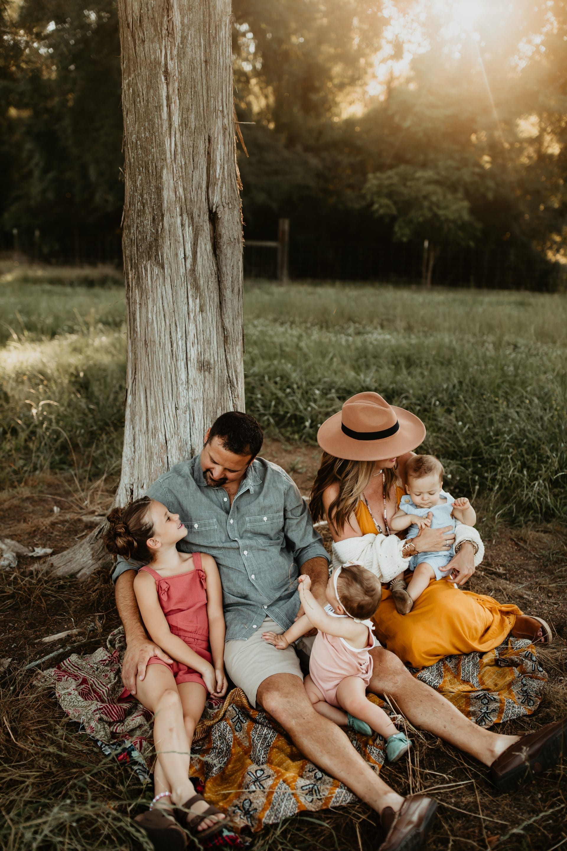 A family is sitting under a tree on a blanket in a field.