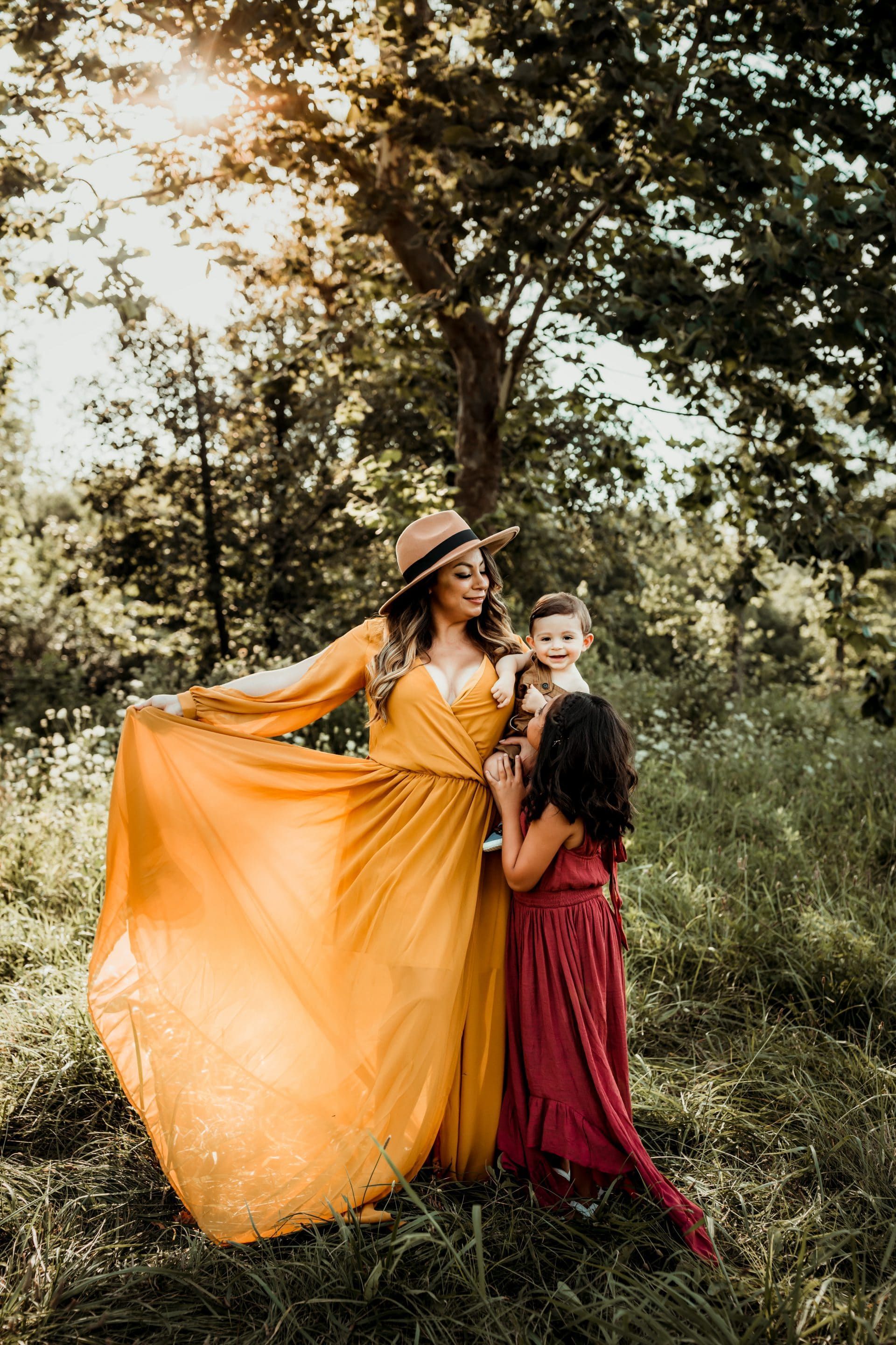 A woman in a yellow dress is standing in a field with two children.