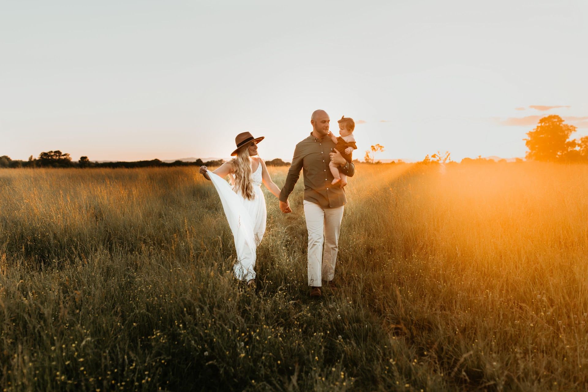 A family is walking through a field at sunset.