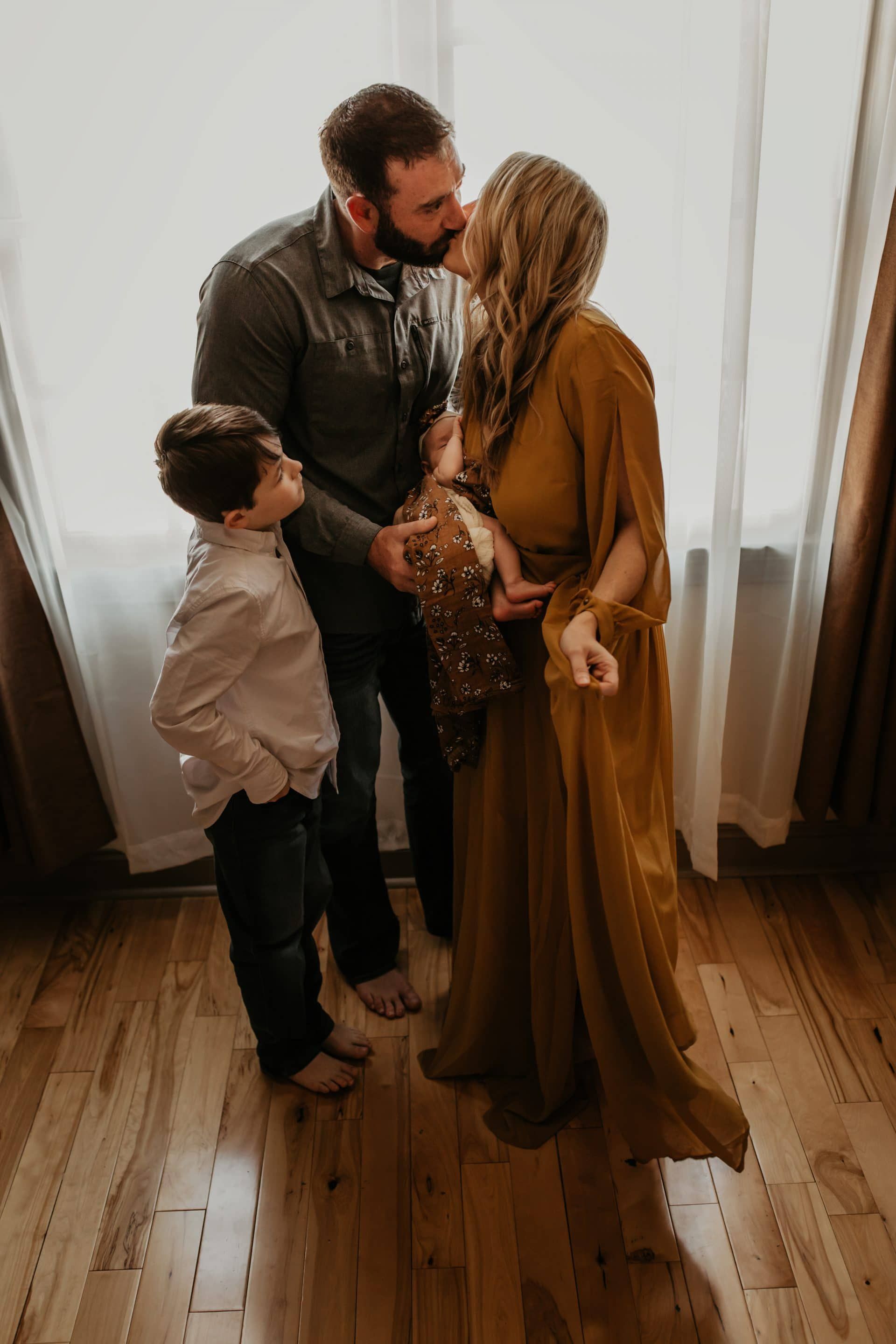 A man is kissing a pregnant woman on the cheek while a boy looks on.