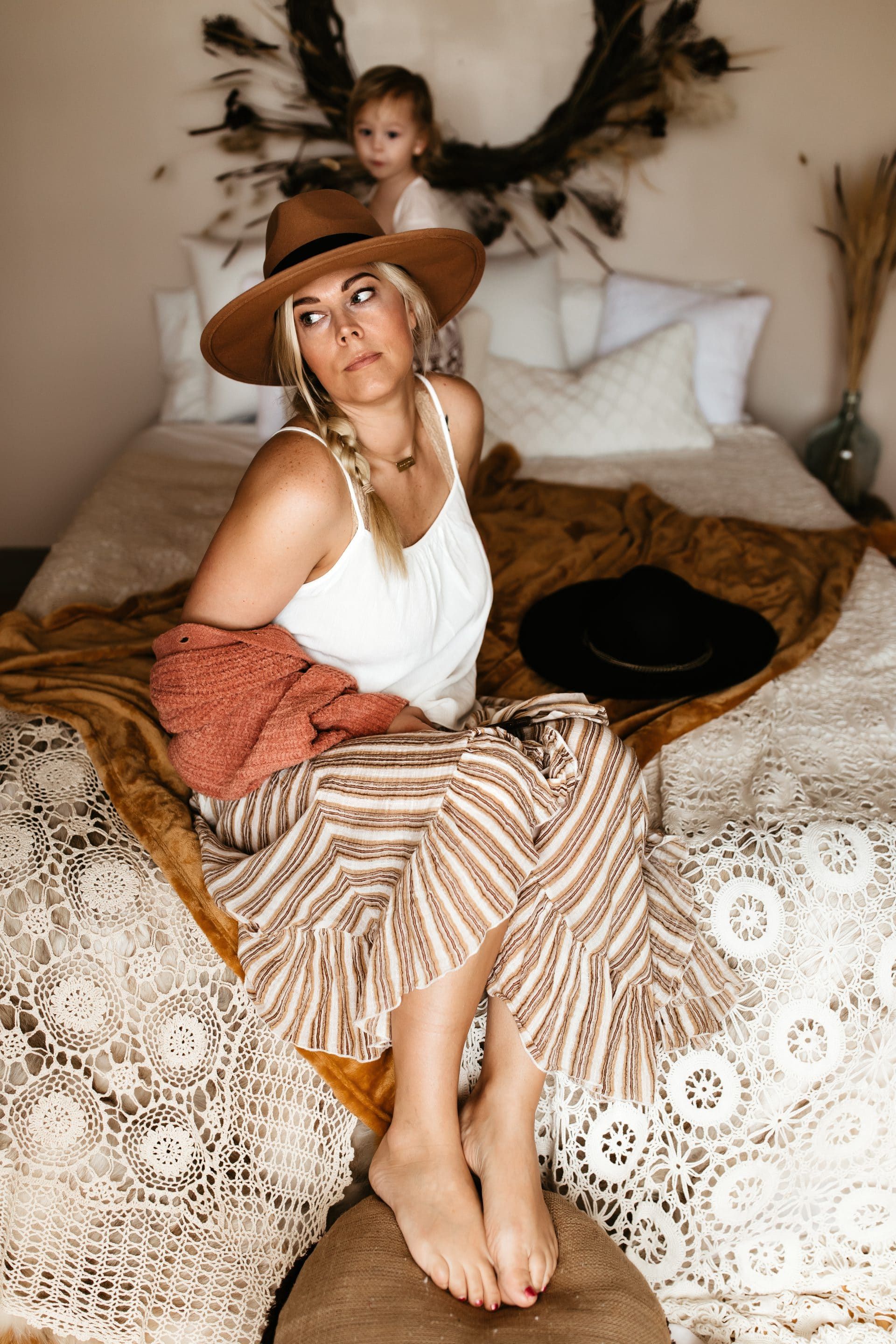 A woman in a hat is sitting on a bed next to a little girl.