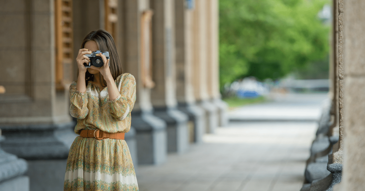 A woman in a dress is taking a picture with a camera.