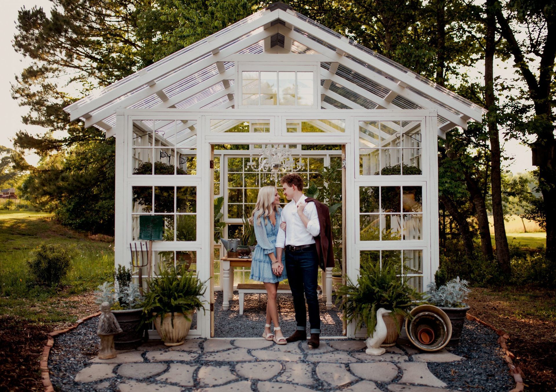 A man and woman are standing in front of a greenhouse holding hands.