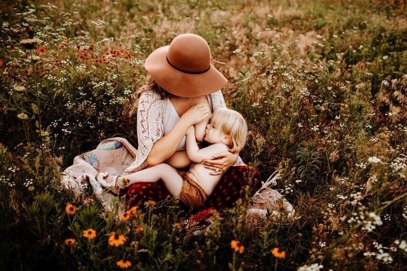 A woman is breastfeeding a baby in a field of flowers.