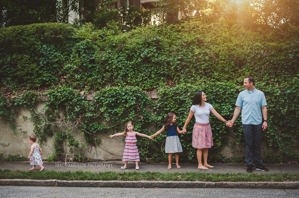 A family is standing on the sidewalk holding hands.