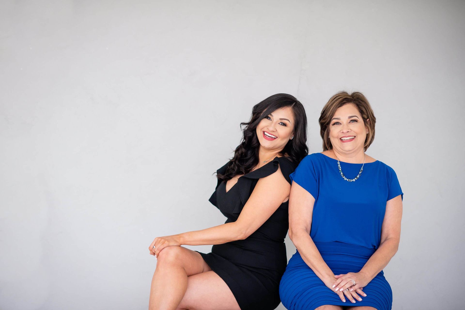 Two women in blue dresses are sitting next to each other and smiling.