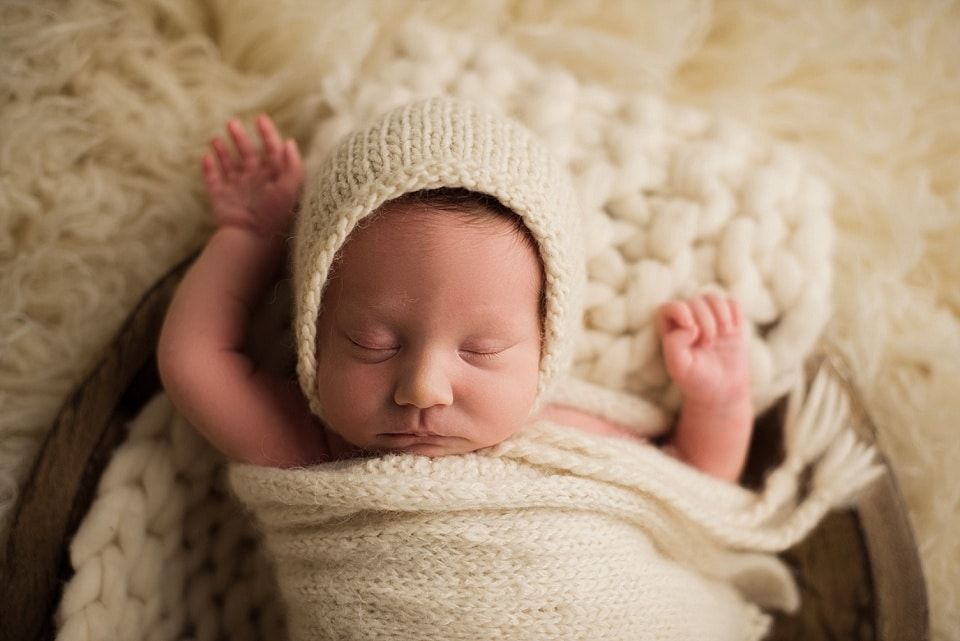 A newborn baby is wrapped in a white blanket and wearing a white hat.