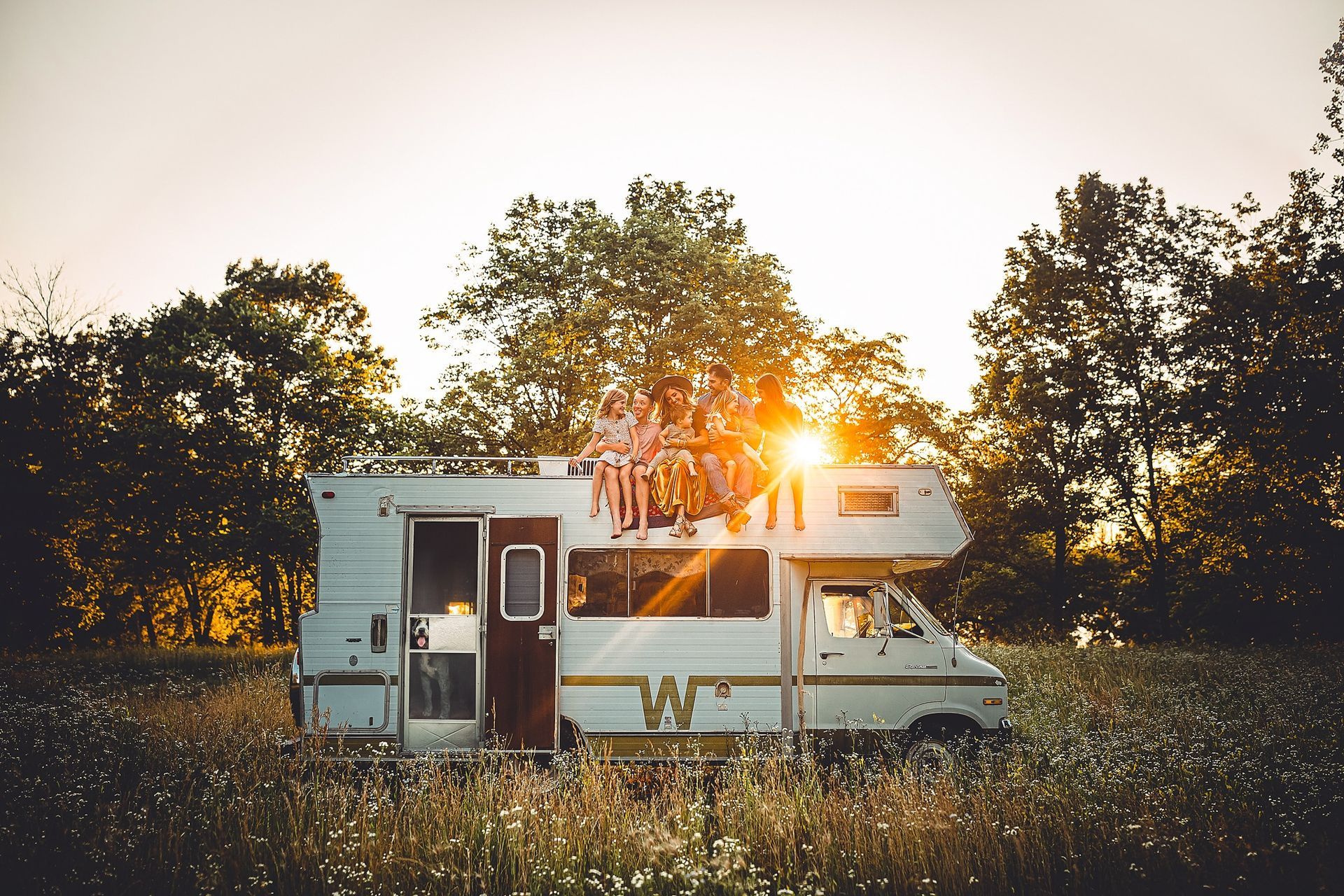 A rv is parked in a field with the sun shining through the trees