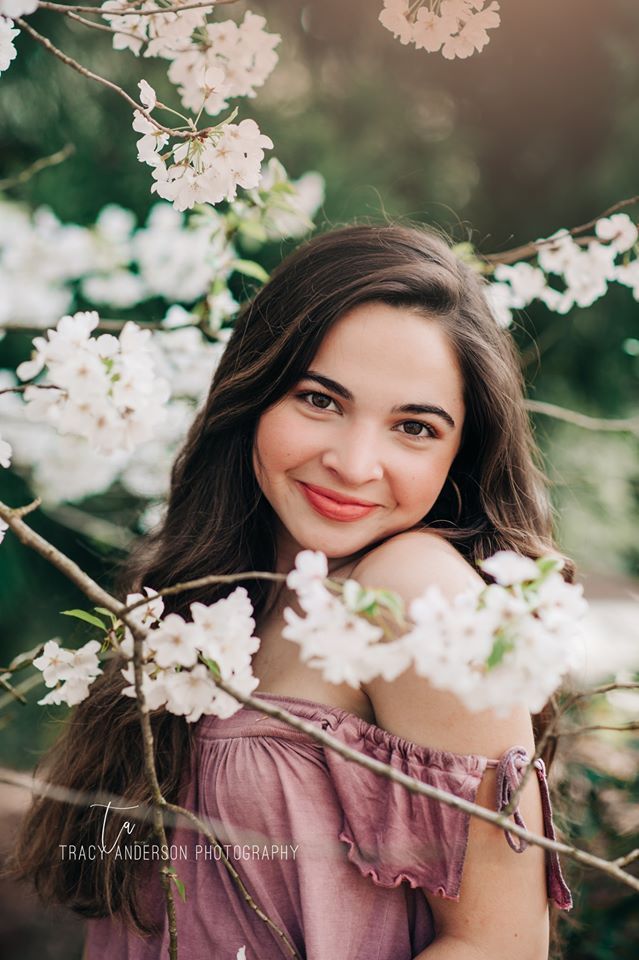 A young woman is standing in front of a tree with white flowers.