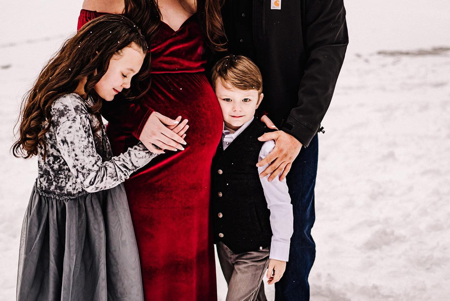 A pregnant woman is standing in the snow with her husband and two children.